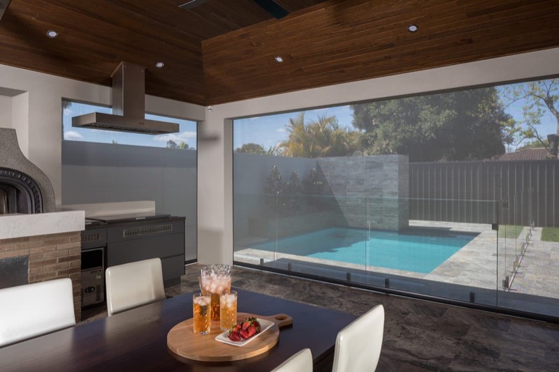 Alfresco dining table set with drinks, looking out through the open side to a pool