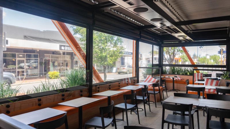 Interior of a venue with bench seating and stools looking out to the street through glazing