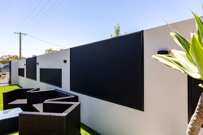 Dark outdoor blind on a white wall beside a planted garden bed