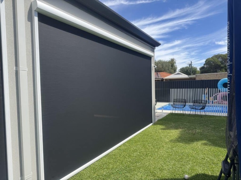 Large dark outdoor blind lowered on a house with a pool and lawn behind