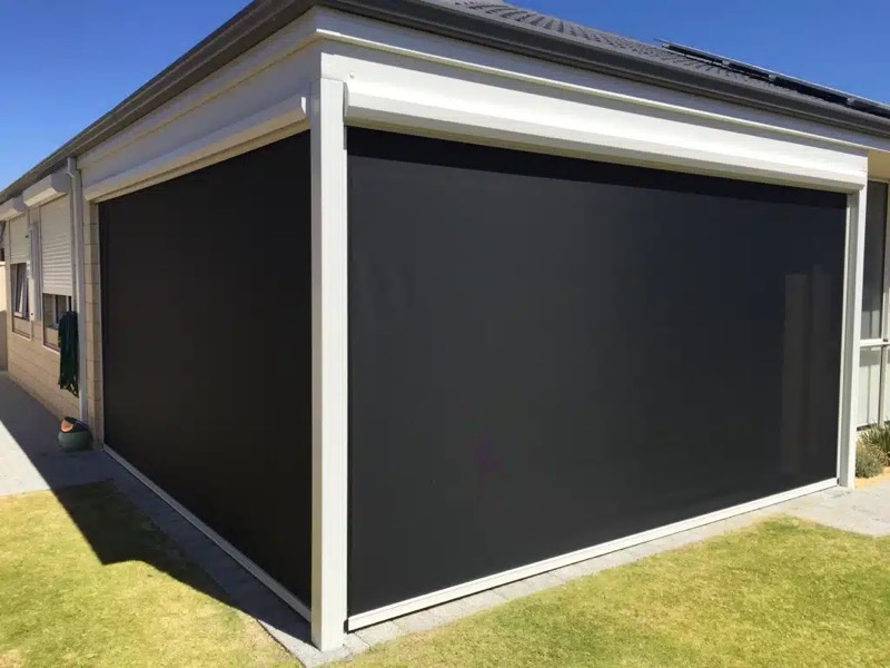 Two outdoor blinds lowered on the corner of a house facing a lawn