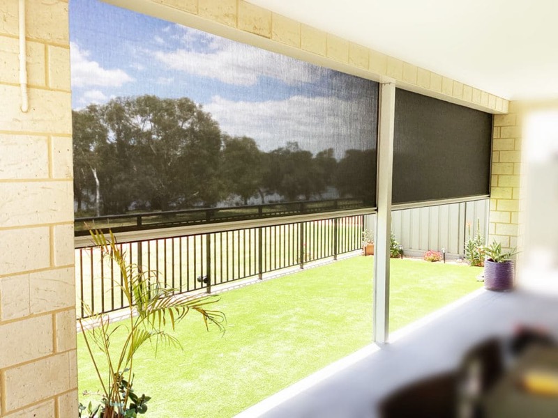 Outdoor blind lowered over a patio, lawn and fence beyond