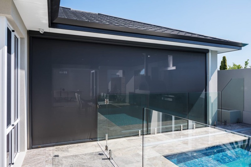 Dark outdoor blind lowered on a rendered modern home beside a swimming pool