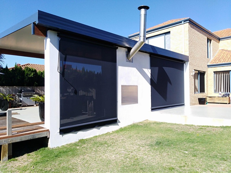 House exterior with outdoor blinds lowered across a covered area, lawn in front